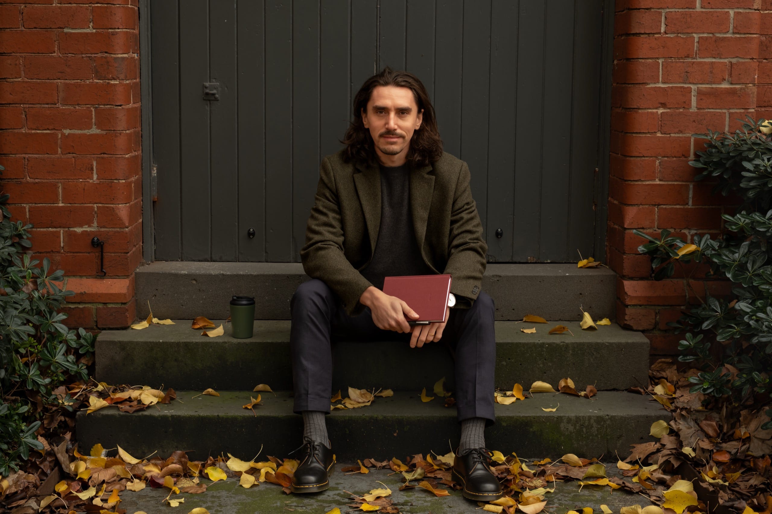 Patryk Dymon, founder of be still, seated on brick steps holding the burgundy A5 journal
